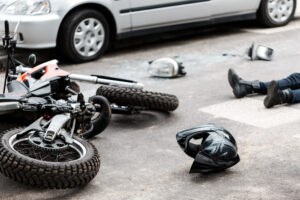 Motorcycle damaged and lying in front of a car with a person on the ground getting ready to call a Motorcycle Accident Lawyer Houston, TX